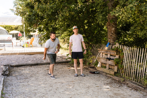 Deux hommes jouent à la pétanque sous un arbre au Flower Camping La Sténiole, Grand Est, France.