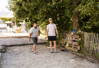 Zwei Männer spielen Petanque unter Bäumen im Flower Camping La Sténiole Ferienpark in Grand Est, Frankreich.