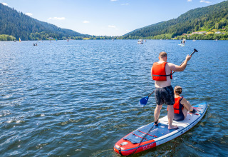 Two people paddleboarding on a serene lake near Granges-Aumontzey, surrounded by forested hills.