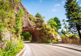 Scenic road near Granges-Aumontzey, Grand Est, France, featuring a rock arch tunnel and lush greenery.