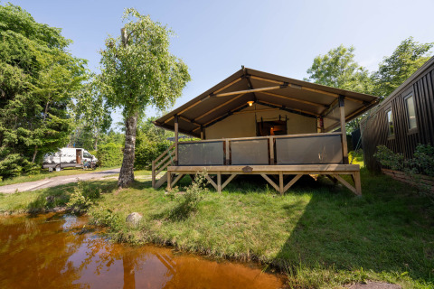 De safaritent Tente Kenya staat op gras naast een vijver, omringd door natuur en een camper in de verte.