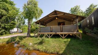 De safaritent Tente Kenya staat op gras naast een vijver, omringd door natuur en een camper in de verte.
