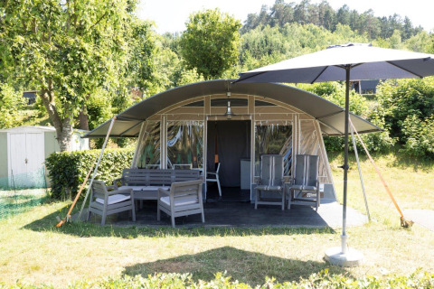 Vista frontale del Nommerlayen Lodge de Luxe con patio, mobili da giardino e ombrellone al Camping Nommerlayen in Lussemburgo.