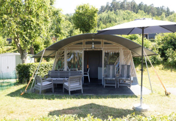 Vista frontal de Nommerlayen Lodge de Luxe con terraza, muebles de jardín y sombrilla en Camping Nommerlayen, Luxemburgo.