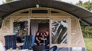 Family smiling in front of Echternacherbrück Lodge tent, with chairs and table outside, enjoying camping.