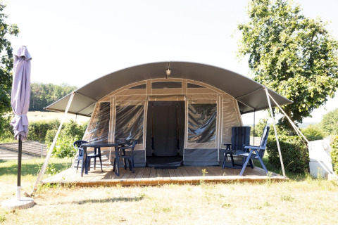 Nommerlayen Lodge en Camping Nommerlayen, Luxemburgo, con terraza sombreada, sillas y mesa al aire libre.