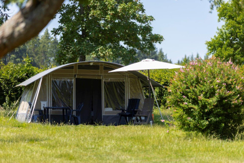 Großes Zelt mit Gartenmöbeln und Sonnenschirm im Grünen bei Auf Kengert Lodge in Luxemburg im Sommer.