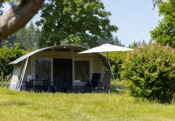 Tenda con mobili da esterno e ombrellone sul prato presso Auf Kengert Lodge ad Auf Kengert, Lussemburgo.