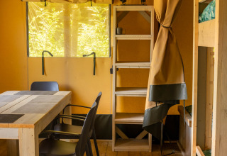 Indvendig billede af en safari telt med træmøbler, stole og køjeseng på Flower Camping La Sténiole i Frankrig.