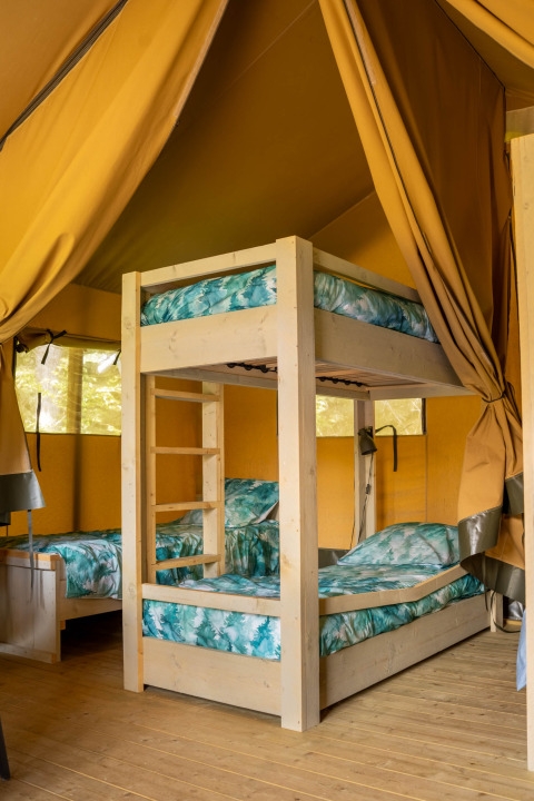 Indretning i en safari telt med køjeseng og enkelt senge på Flower Camping La Sténiole i Frankrig.