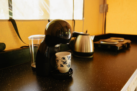 Sort kaffemaskine med en kop på køkkenbord i en safaritelts køkken på Flower Camping La Sténiole, Frankrig.