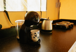 Sort kaffemaskine med en kop på køkkenbord i en safaritelts køkken på Flower Camping La Sténiole, Frankrig.