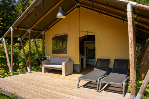Safari-telt med trædæk, sofa og liggestole på Flower Camping La Sténiole i Frankrig, omgivet af natur.
