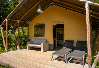 Safari-telt med trædæk, sofa og liggestole på Flower Camping La Sténiole i Frankrig, omgivet af natur.
