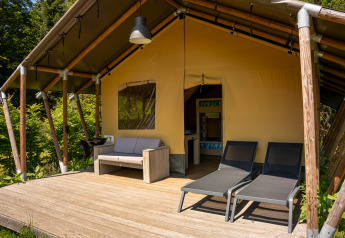 Tenda safari con terrazza in legno, divano e lettini al Flower Camping La Sténiole in Francia.