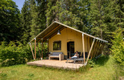 Tenda safari al Flower Camping La Sténiole in Francia, immersa nel bosco con una persona che si rilassa sul patio.