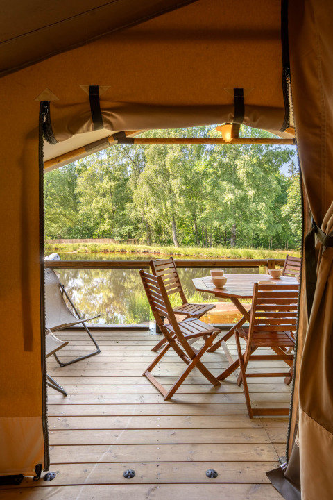 Vista dal terrazzo di una tenda safari con tavolo e sedie in legno sul lago a Flower Camping La Sténiole.