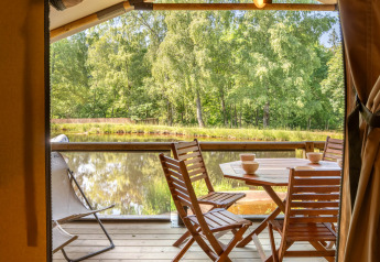 Blick von einem Safari-Zelt mit Holzmöbeln auf einen See und grüne Wälder im Flower Camping La Sténiole.
