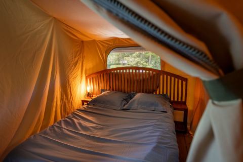 Interieur van safaritent Tente Kenya met groot bed en nachtkastjes bij Flower Camping La Sténiole, Frankrijk.