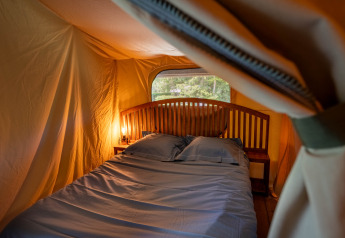 Interior de la tienda safari Tente Kenya con una cama y mesitas de noche en Flower Camping La Sténiole, Francia.