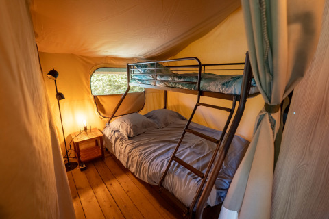Indvendig udsigt af et safari telt med køjeseng og natbord på Flower Camping La Sténiole i Frankrig.