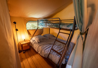 Innenansicht eines Safari-Zeltes mit Etagenbett und Nachttisch im Flower Camping La Sténiole in Frankreich.