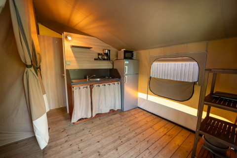 Interno di una tenda safari con angolo cottura, frigorifero e pavimento in legno a Flower Camping La Sténiole, Francia.