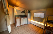 Interior of a safari tent with kitchenette, fridge, and wooden floor at Flower Camping La Sténiole, France.