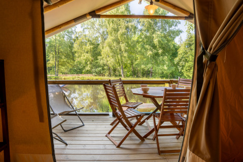 Udsigt fra safari telt Tente Kenya med træterrasse og havemøbler ved søen på Flower Camping La Sténiole, Frankrig.
