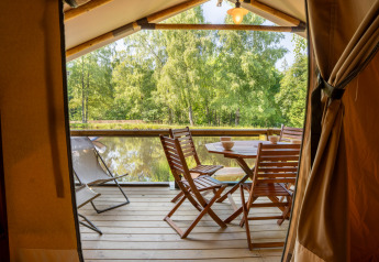 Vista desde la tienda safari Tente Kenya con terraza de madera y muebles junto al lago en La Sténiole, Francia.