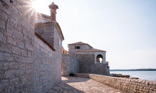 Zonnige stenen muur en historische gebouwen aan zee bij Novigrad, Istrië, Kroatië.