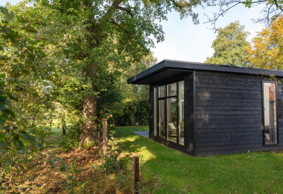 Moderna cabaña negra Wellness Boutique baby, situada junto a árboles altos y césped verde exuberante.