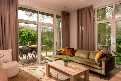 Sala de estar con sofá verde y grandes ventanales en lodge Wellness Boutique de Holiday Park Mölke, Países Bajos.