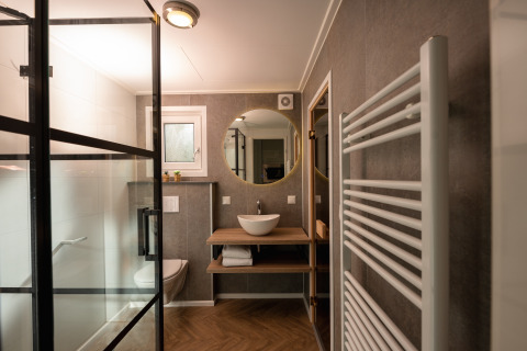 Baño moderno en Wellness Boutique baby en Holiday Park Mölke, Países Bajos, con ducha de vidrio y espejo redondo.