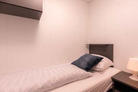 Cama individual con sábanas blancas y cojín gris en Wellness Boutique baby en Holiday Park Mölke, Países Bajos.