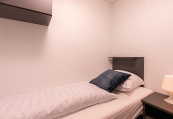 Letto singolo con lenzuola bianche e cuscino grigio al Wellness Boutique baby nel Holiday Park Mölke, Paesi Bassi.