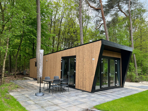 Moderne Just Nature Light-lodge med træfacade, store vinduer og terrasse, omgivet af frodig skov.