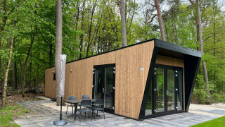 Strakke Just Nature Light-lodge in hout met grote ramen en een terras, midden in het groene bos.