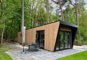 Moderna lodge Just Nature Light in legno con ampie vetrate e patio, immersa in una rigogliosa foresta.
