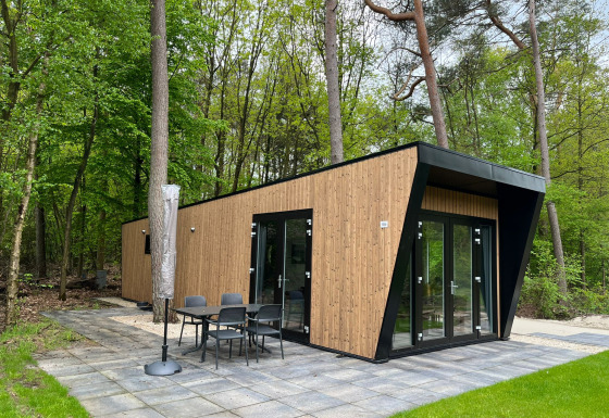 Moderne Just Nature Light-lodge med træfacade, store vinduer og terrasse, omgivet af frodig skov.