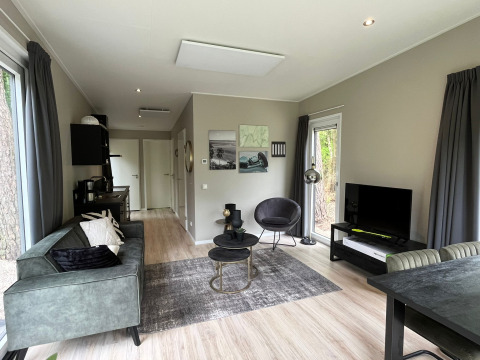 Moderne stue i Just Nature Light-lodge ved De Hooge Veluwe, Holland, med sofa, tv og store vinduer.