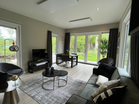 Moderne lodge-stue med store vinduer, stilfuld indretning og udsigt til grøn natur i Holland.
