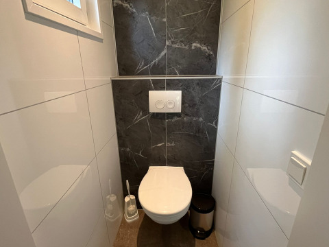 Moderne toilet med væghængt toilet, sort flisebaggrund og hvid indretning på Just Nature Light, De Hooge Veluwe.