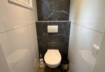 Bagno moderno con wc sospeso, parete con piastrelle nere e arredamento bianco presso Just Nature Light, De Hooge Veluwe.