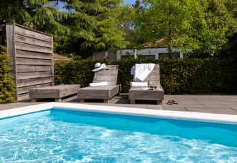 Zwei Liegestühle mit Handtüchern und Getränken am Pool eines Glamping-Unterkunfts unter Bäumen.