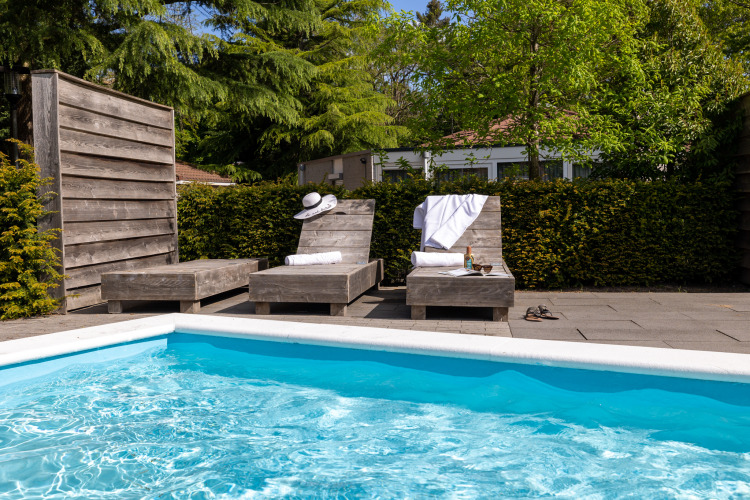 Zwei Liegestühle mit Handtüchern und Getränken am Pool eines Glamping-Unterkunfts unter Bäumen.