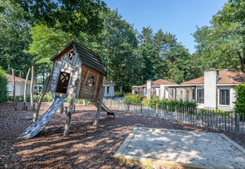 Aire de jeux avec cabane en bois et toboggan devant des hébergements glamping modernes et verdoyants.