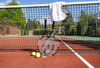 Tennisketsjere, bolde, en flaske vand og et håndklæde på nettet på en tennisbane ved glamping.