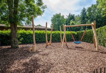 Aire de jeux avec balançoire et structures en bois sur copeaux, dans un hébergement de glamping nature.