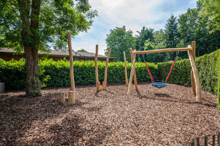 Playground with a swing and wooden climbing posts on a bark-covered area at a glamping accommodation.